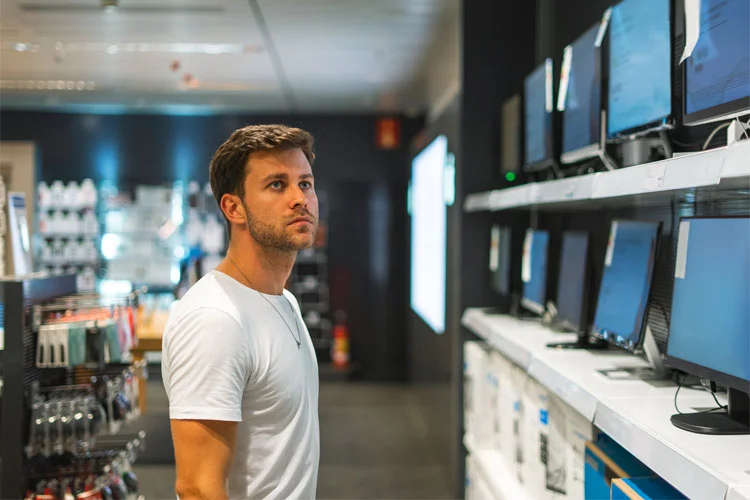 Homme songeur choisissant un ordinateur en magasin